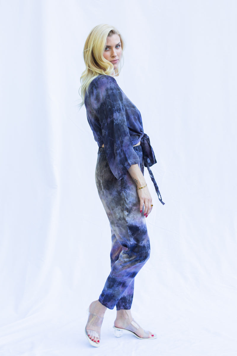 Side view of woman wearing matching set featuring georgette wrap top in cosmica, a purple tie dye color.