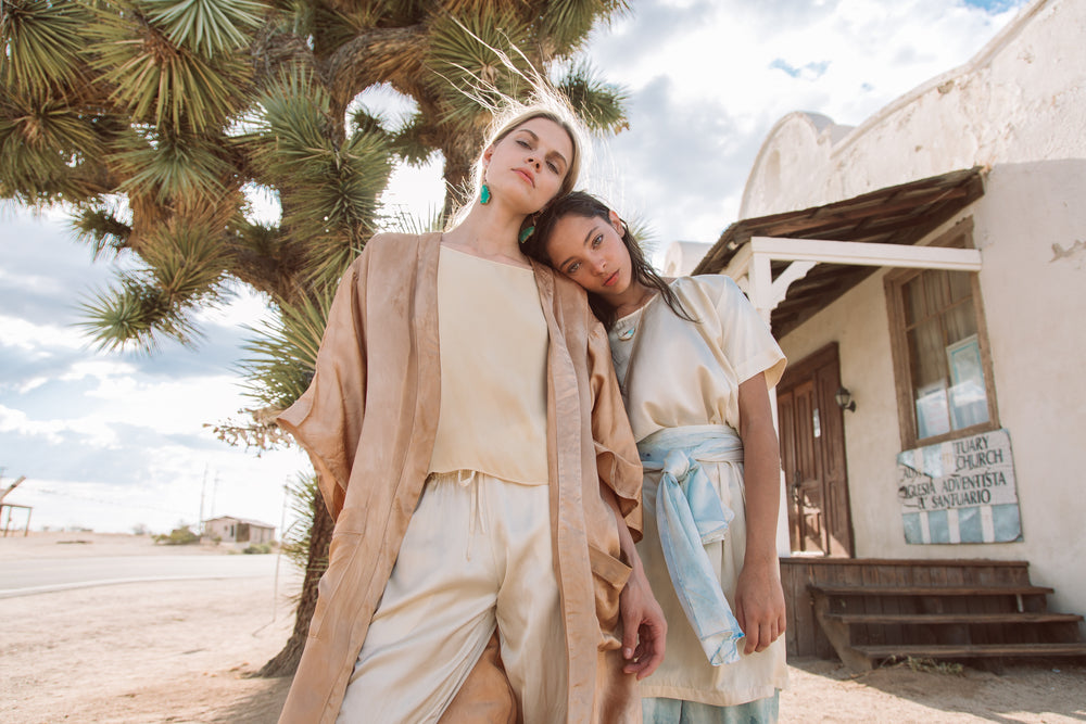 two models in desert landscape wearing silk duster, silk top, silk pants, silk dress, and silk scarf
