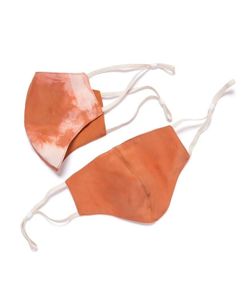 two face masks showing both sides of reversible silk face mask with one side tie dyed orange and cream and the other orange. Each mask has cream color elastic bands.