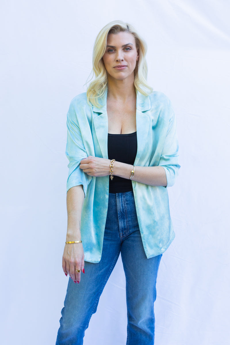 Front view of woman wearing silk blazer in turquoise blue pulling up sleeve. 