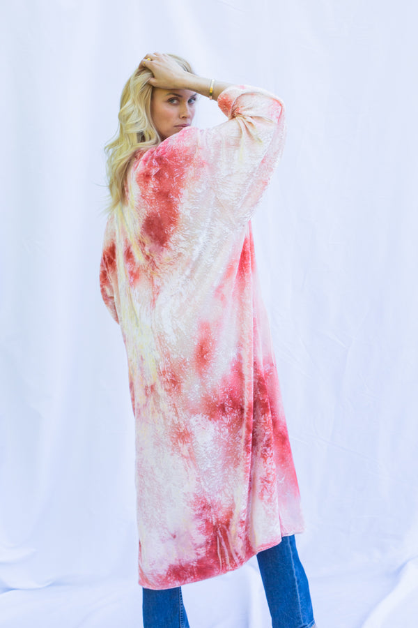 Side view of blond woman looking over her shoulder wearing velvet duster in heavenly pink. Duster has marbled tie tie markings. 