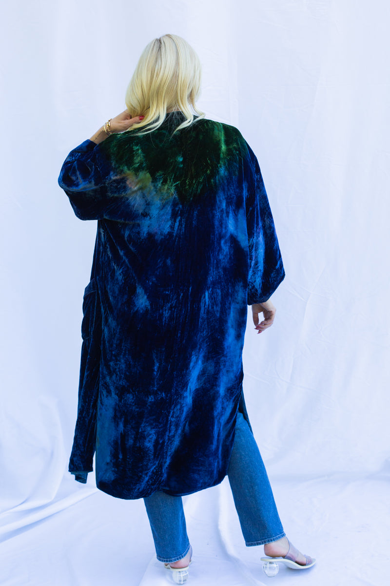 Back view of woman wearing ceremony duster. Duster is green at collar and shoulders fading into a deep blue.