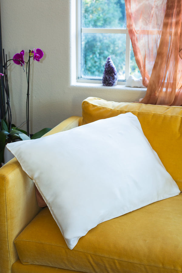 Silk cream colored pillowcase on yellow velvet couch with orchid in background.