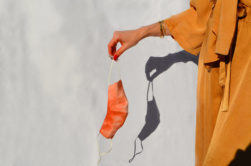 model holding out reversible silk face mask in tie dyed orange and cream 